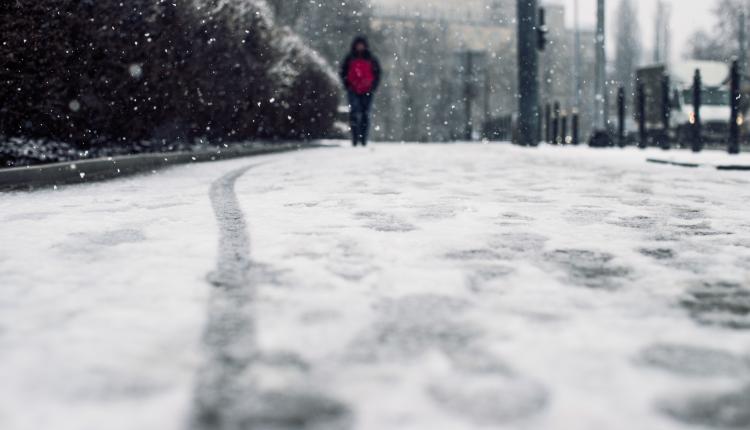 Low angle shot of a person walking on the snow covered sidewalk under the snow