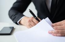 Closeup of business man signing document at office desk