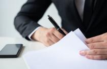 closeup-of-business-man-signing-document-at-office-desk-scaled