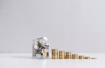 glass-jar-full-of-money-in-front-of-decreasing-stacked-coins-against-white-background_23-2147919228