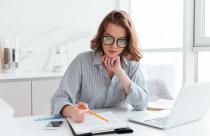 Young concentrated businesswoman in glasses and striped shirt wo