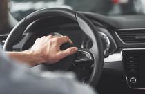 Man's big hands on a steering wheel while driving a car.