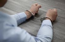 selective-focus-shot-of-male-hands-in-handcuffs-on-a-wooden-table