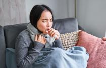 Asian woman coughing, feeling sick, sitting under blanket with scard in cold apartment, saving on heating this winter, catching flu