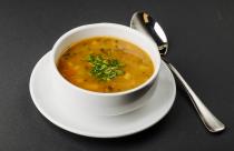 lentil-soup-with-mixed-ingredients-and-herbs-in-a-white-bowl-with-a-spoon