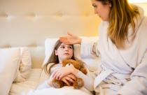 Mother checking fever of her daughter in bedroom