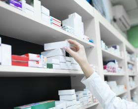 Closeup view of pharmacist hand taking medicine box from the shelf in drug store.