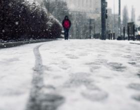 Low angle shot of a person walking on the snow covered sidewalk under the snow