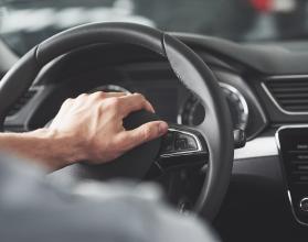 Man's big hands on a steering wheel while driving a car.