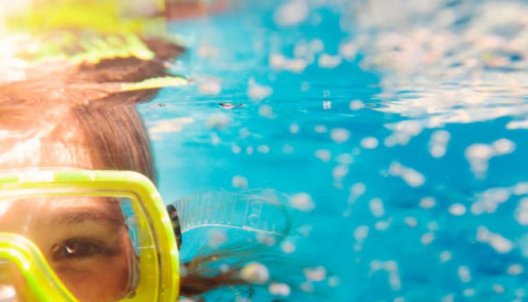 Little girl in colorful swimming mask smiling looking at camera under water