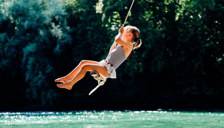 Little girl having fun on rope swing above river.