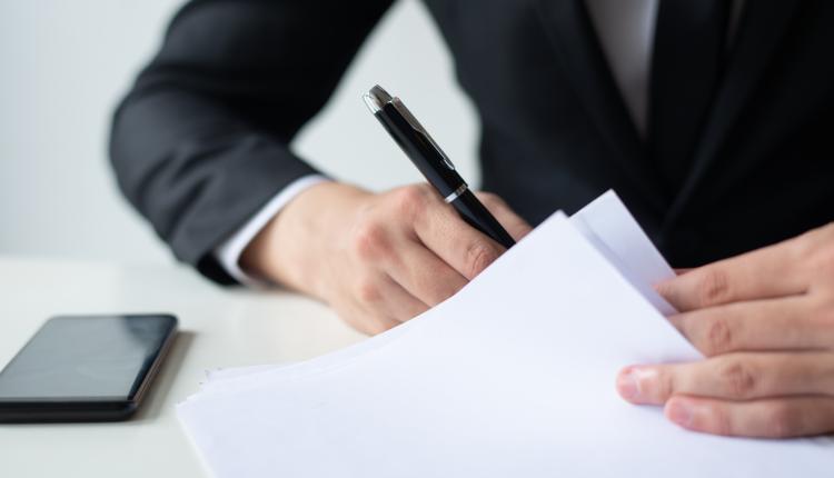 Closeup of business man signing document at office desk