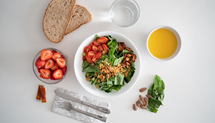 Bowl of salad with herbs, tomatoes, and almonds on the table with strawberries and bread slices