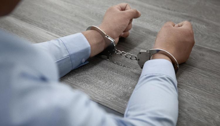 selective-focus-shot-of-male-hands-in-handcuffs-on-a-wooden-table