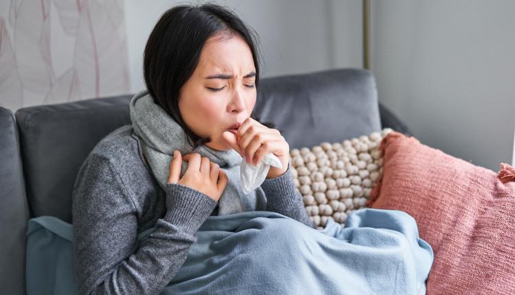 Asian woman coughing, feeling sick, sitting under blanket with scard in cold apartment, saving on heating this winter, catching flu