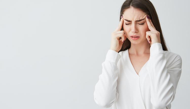 Young beautiful brunette businesswoman holding fingers on temples frowning from pain over white background. Headache.