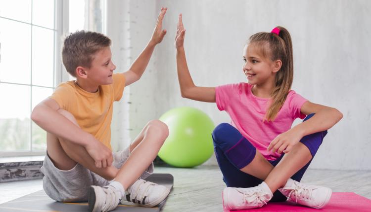 boy-and-girl-sitting-on-exercise-mat-giving-high-five