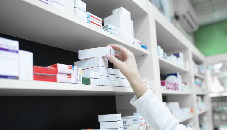 Closeup view of pharmacist hand taking medicine box from the shelf in drug store.