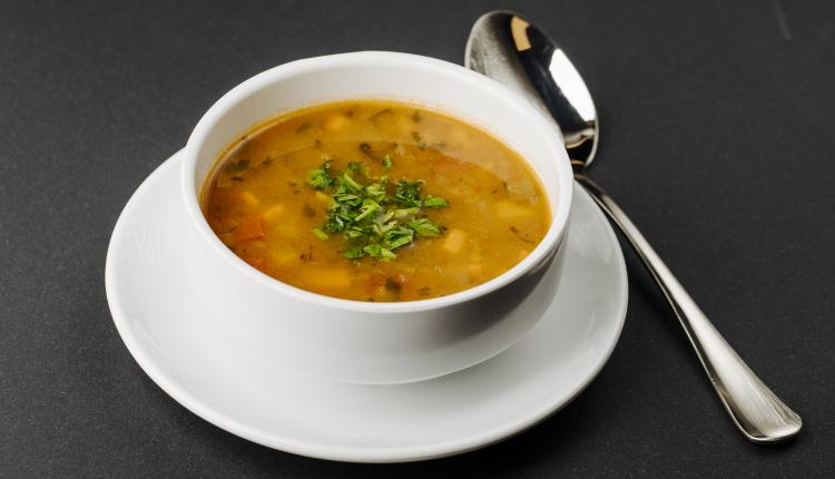 lentil-soup-with-mixed-ingredients-and-herbs-in-a-white-bowl-with-a-spoon