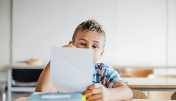 boy-sitting-desk-holding-sheet_23-2147659426