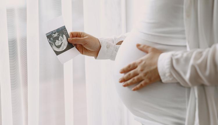 Pregnant woman stands by the window and looks at photo