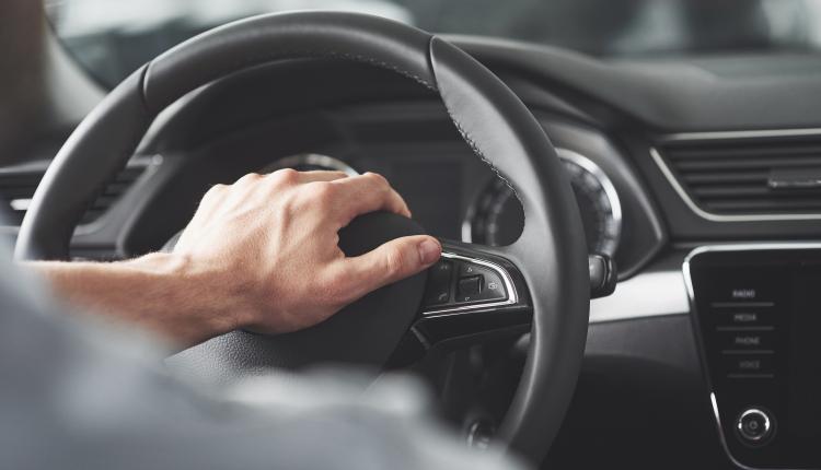 Man's big hands on a steering wheel while driving a car.