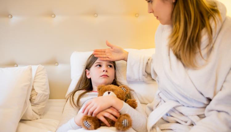 Mother checking fever of her daughter in bedroom